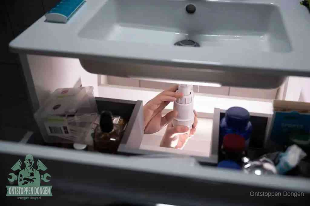 Een pompfles met zeep boven een wastafel, de heet water en afwasmiddel-methode om een vetprop in de afvoer los te maken in Dongen