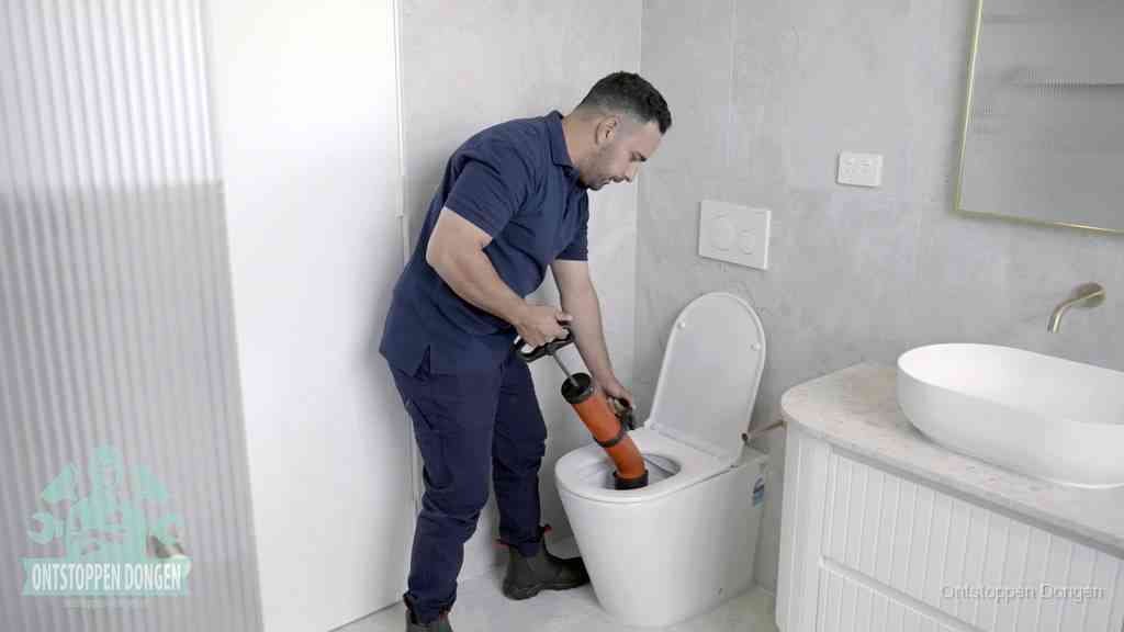 Een monteur buigt over een wandcloset en duwt met de hand een persluchtontstopper in de toiletpot om de verstopping handmatig los te maken in Dongen