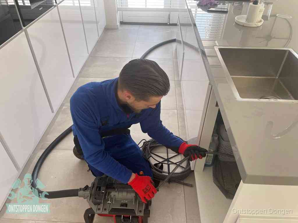 Een monteur ontstopt de keukenafvoer onder de spoelbak met een elektrische veermachine in Dongen