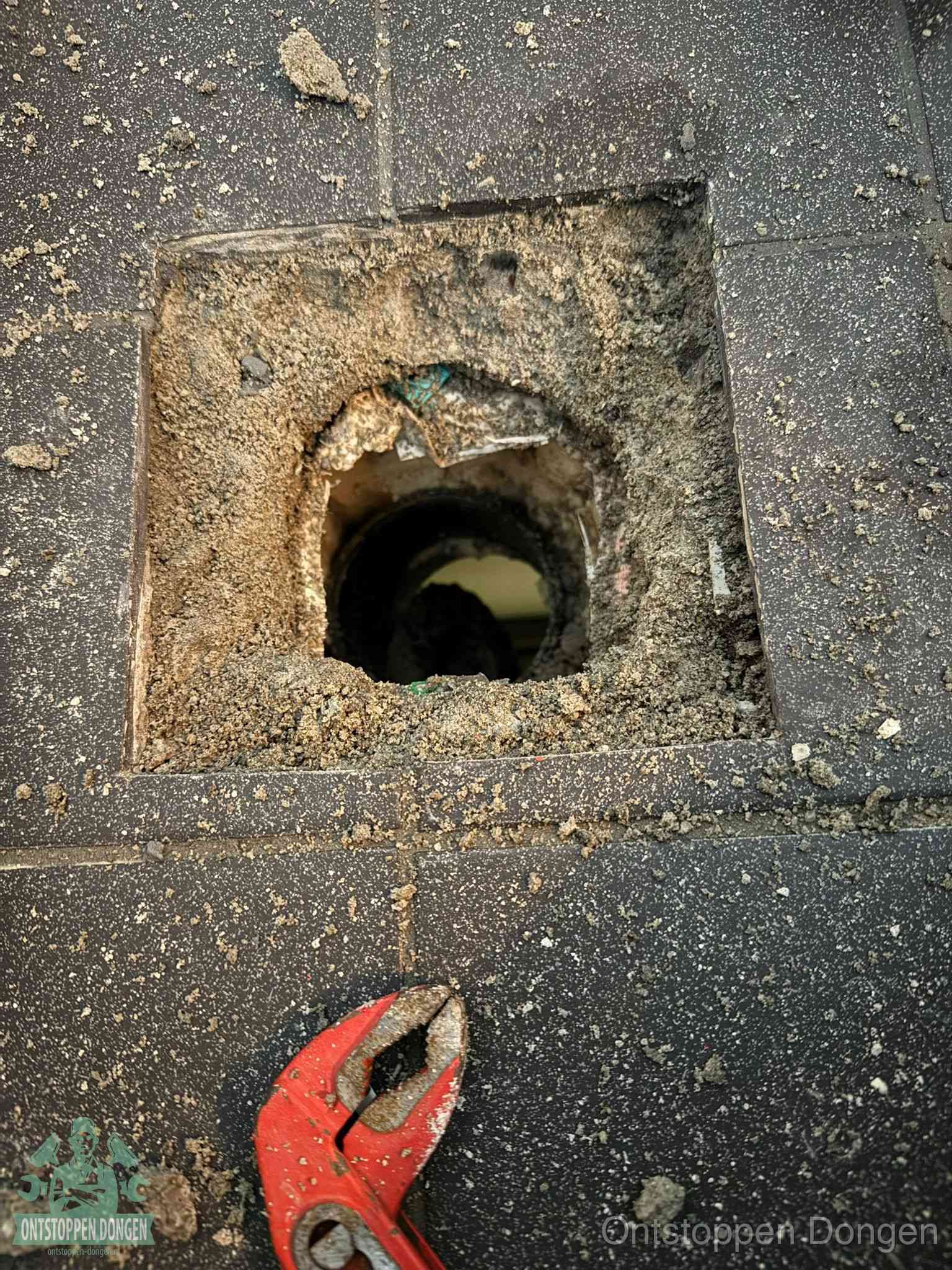 Een geopend rioolputje in een betontegelvloer met losgemaakt rooster en een zichtbare ronde afvoerbuis, het achterhalen waar de afvoerverstopping zit in Dongen