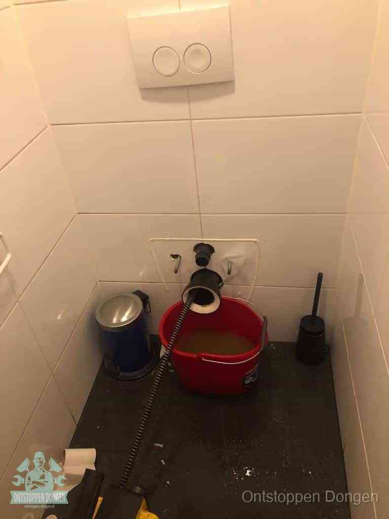 Een ontstopte wand-wc met verwijderde toiletpot waar een ontstoppingsveer in de wanduitgang verdwijnt, het achterhalen waar de verstopping zit in Dongen