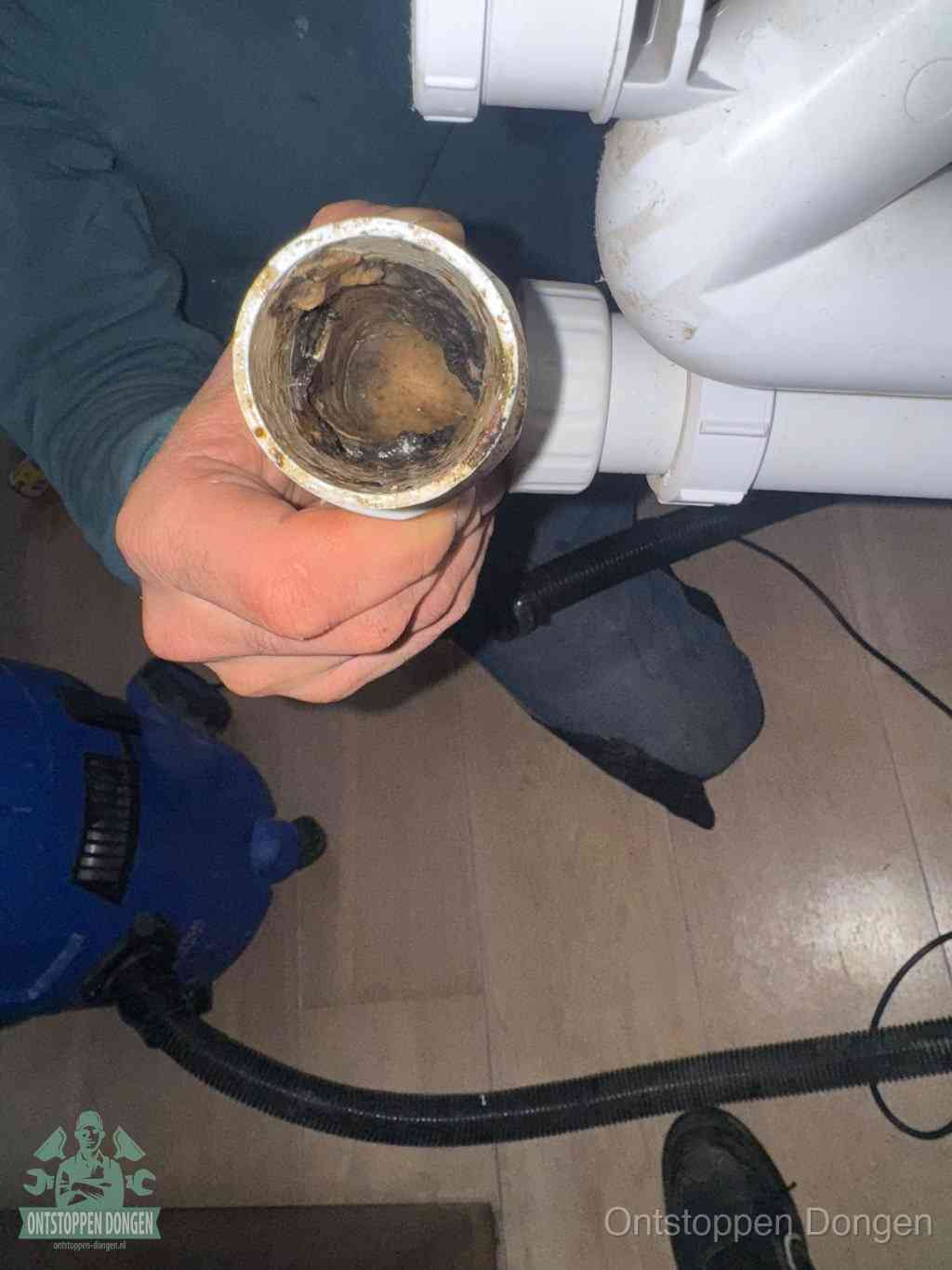 Een hand houdt een losgekoppeld PVC-afvoerbuisstuk vast dat van binnen volledig is dichtgeslibd met vet, vuil en aanslag, de meest voorkomende oorzaak van een verstopte afvoer in Dongen