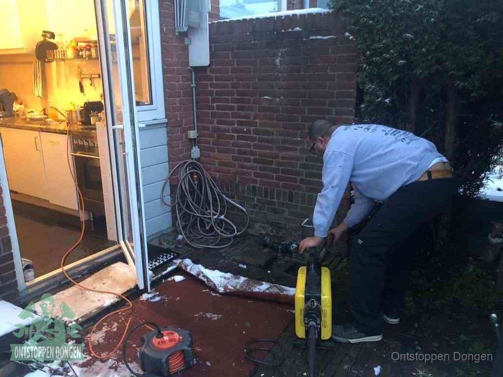 Een monteur werkt buiten bij een open riool-/grondput met een elektrische ontstoppingsmachine om een verborgen afvoerprobleem op te sporen in Dongen