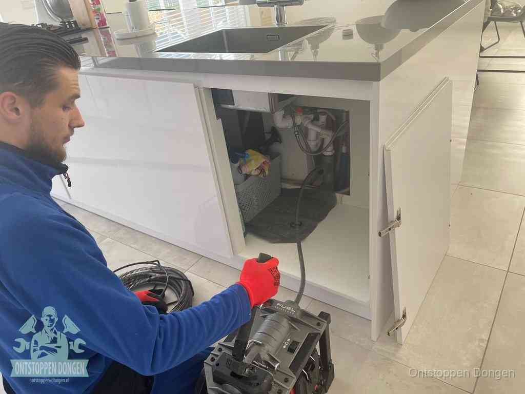 Monteur ontstopt met een veermachine een verstopte afvoer onder de gootsteen in Dongen