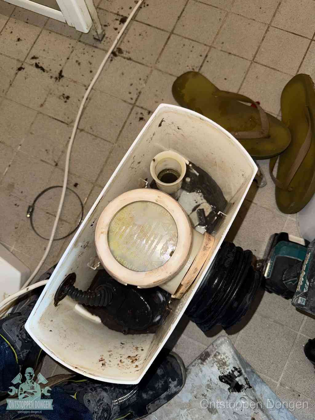 Een gedemonteerde toiletpot op de vloer met ontstoppingsveer en gereedschap ernaast, het verwijderen van een vastzittend voorwerp uit de wc in Dongen