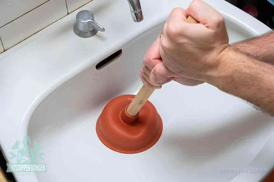 Twee handen gebruiken een rode rubberen plopper op een sanitair-afvoer om het toilet te ontstoppen in Dongen
