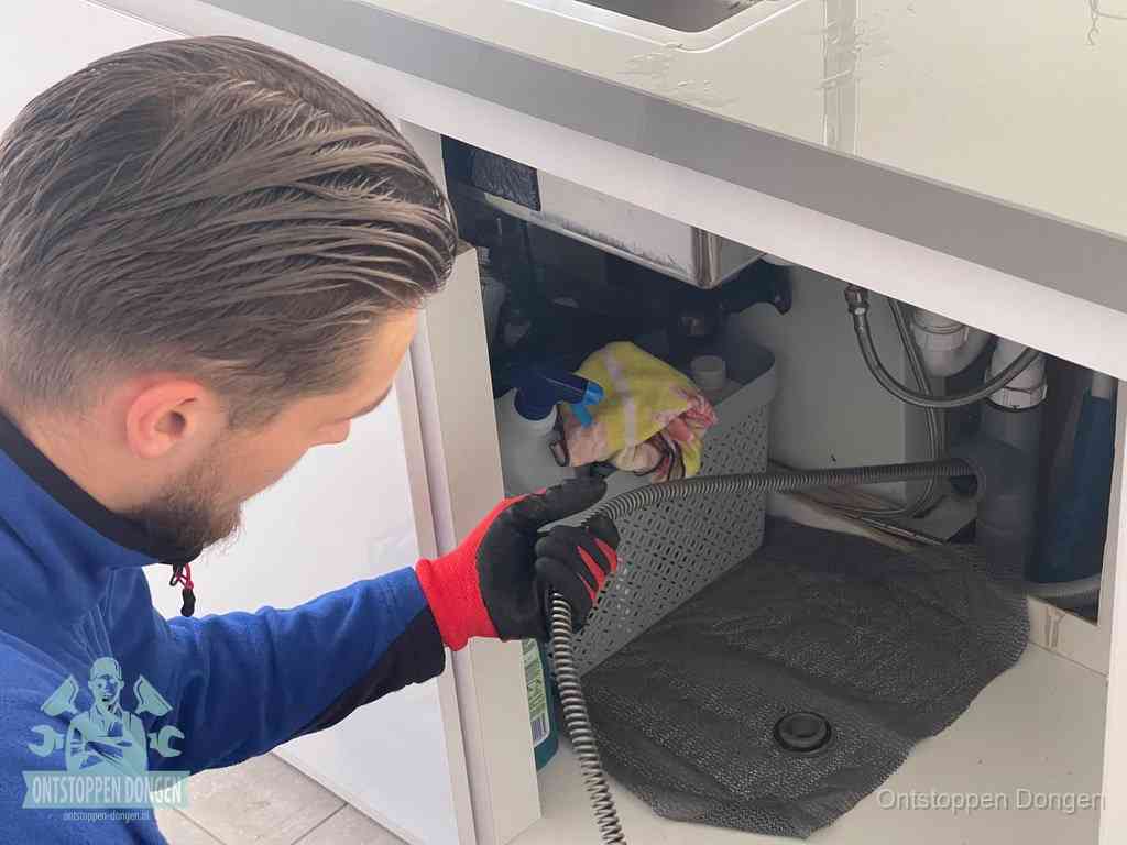 Een monteur voert een flexibele ontstoppingsveer in de afvoer om een verstopping voorbij de bocht van het toilet te bereiken in Dongen