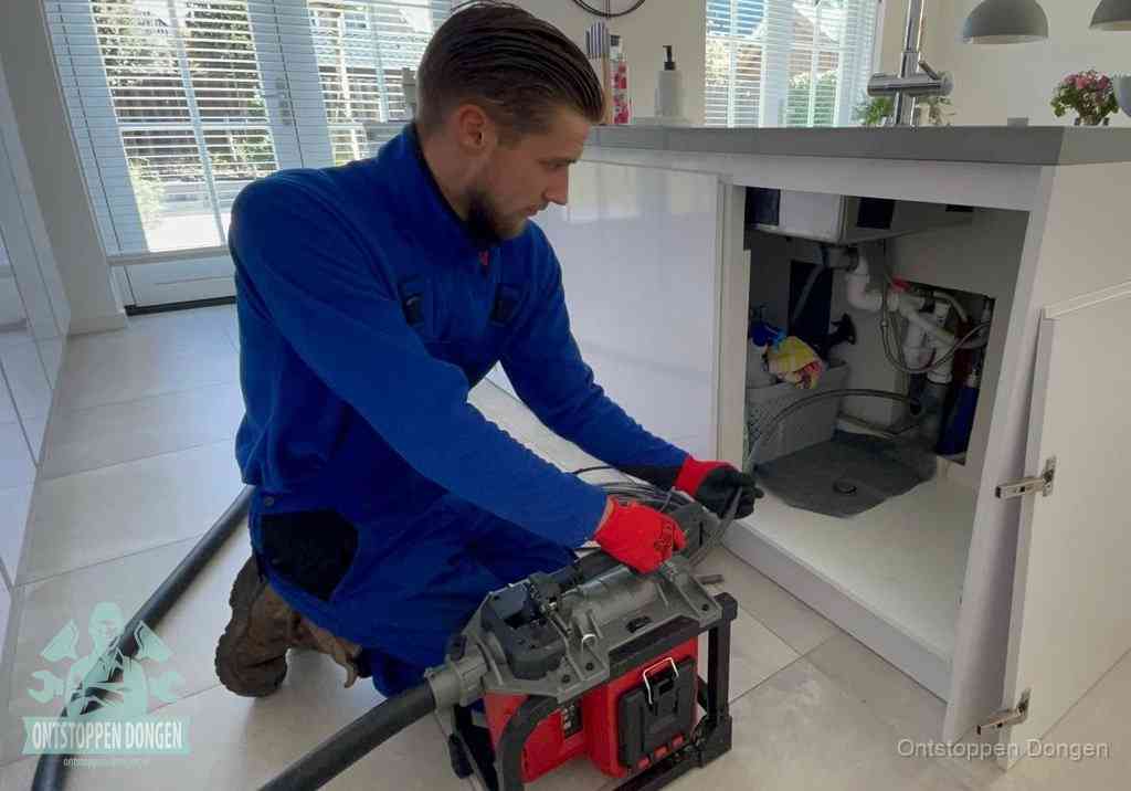Een monteur voert een professionele elektrische ontstoppingsmachine in de afvoer onder de spoelbak tijdens het gootsteen ontstoppen in Dongen