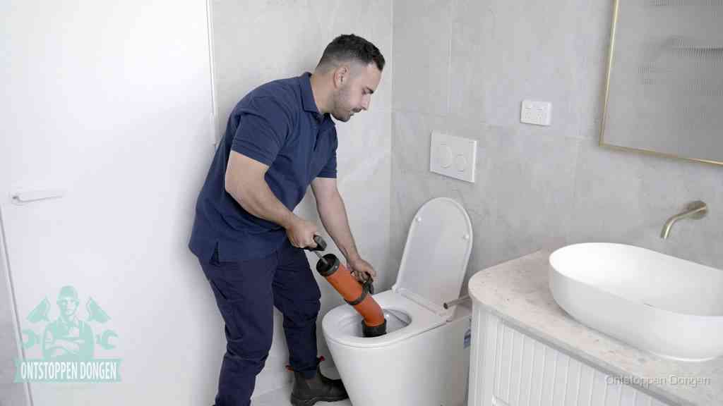 Een monteur gebruikt een handmatige perspomp (toiletontstopper) op een wandcloset tijdens het professioneel wc ontstoppen in Dongen