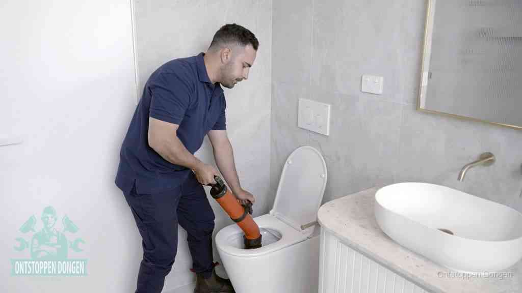 Een man gebruikt een handmatige luchtdruk-ontstopper in een modern betegeld toilet om zelf de wc te ontstoppen in Dongen